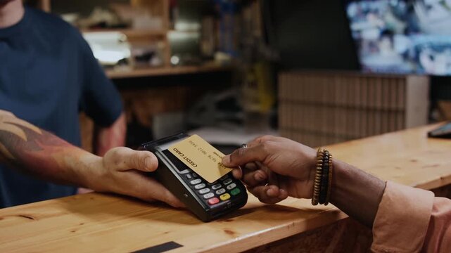 Medium closeup of unrecognizable male customer paying for purchase or service with credit card, tapping it on terminal