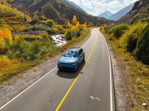 Ala Archa, Kyrgyzstan - October 13, 2024: A light blue Li Auto L7 SUV is parked on a dirt area beneath a canopy of golden yellow autumn trees with rocky mountains in the background