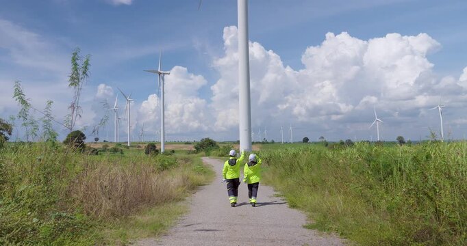 Engineer couple walking on wind farm pathway wearing reflective jacket helmet observing turbine area discussing performance maintenance teamwork concept sustainable energy innovation clean environment