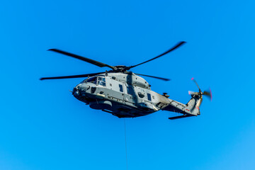 Military helicopter in the air on blue sky background. Gray patrol helix close up. Naval helicopter vehicle flying.