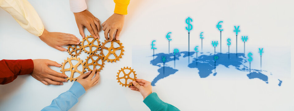 A group of diverse hands gathers around gears, symbolizing teamwork and collaboration in the global economy while highlighting various currencies on a world map. Trope