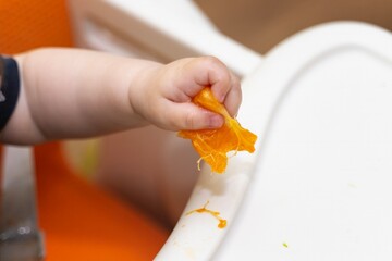 Baby's hand squeezing a mandarin wedge, juice dripping out during first solid food experience