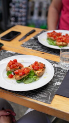 People dining al fresco at Italian restaurant with plates of pasta, pizza, and drinks