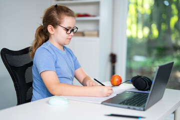 Child learning online with laptop at home. Kid studying using laptop in classroom. Kid student doing homework during online lesson. Kid focused on laptop in homeschooling. Student at desk e-learning.