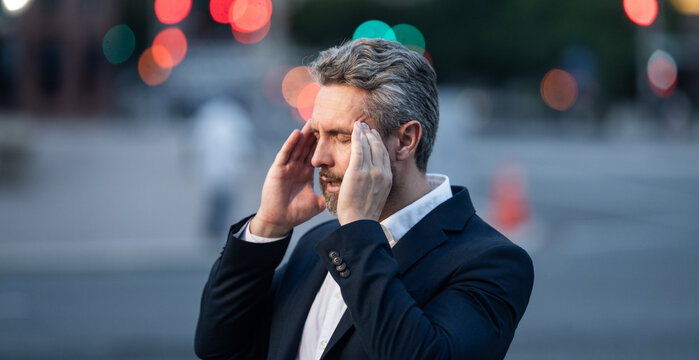 Tired business man suffering from headache outdoor. Man in suit relieving pain, migraine. Business problems. Bankruptcy, financial problem and crisis concept. Millennial man having headache. Migraine