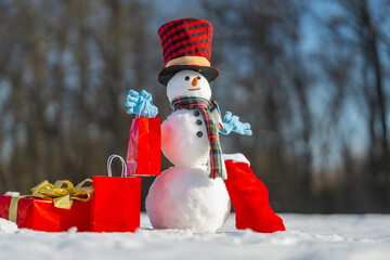 Snowman holding a Christmas gift box on winter background. Snowman with gift on a snowy winter day....