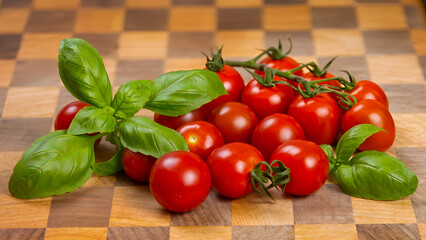 Fresh cherry tomatoes on a vine and green basil on a wooden chessboard