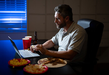 Office worker eating pizza after finishing job. Night mood in office. Freelancer rest in office with beer and snacks. Man relaxation after hard work at office.