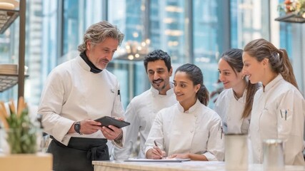 Culinary Team's Collaborative Focus: A team of diverse culinary professionals gathers around, attentively engaged as one reviews digital data for crafting dishes - Powered by Adobe