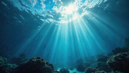 Obraz premium Sunlight beams through clear blue ocean water onto coral reef below. Light rays illuminate sea bottom, creating ethereal underwater scene. Serene deep ocean abyss.