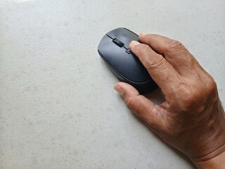 A man's hand holding or using a mouse against a light background. Using a mouse for computer activities.
