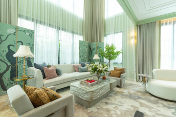 Interior of a luxurious sitting room with bay window sofas and coffee table. White and green tone of vast luxury living room.
