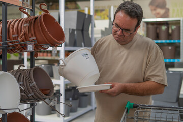 Man shopping for garden pots at a plant store, feeling indecisive about which flower container to purchase