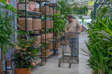 Man shopping for plants and home decor items with a cart in a spacious garden center or nursery retail store
