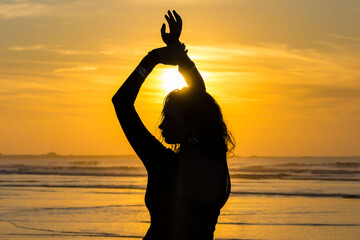 Silhouette of woman dancing on the beach at sunset with sun above the sea.