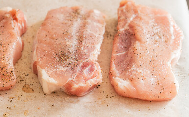 fresh pork chops seasoned with salt and pepper on parchment paper