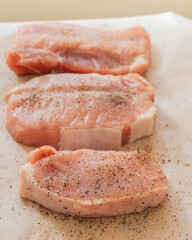 fresh pork chops seasoned with salt and pepper on parchment paper