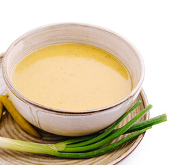 Creamy yellow soup served in a bowl with green onions beside it