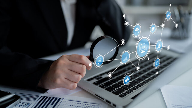 A business professional examines data trends with a magnifying glass on a laptop, surrounded by digital icons that represent modern technology and connectivity. Tessel