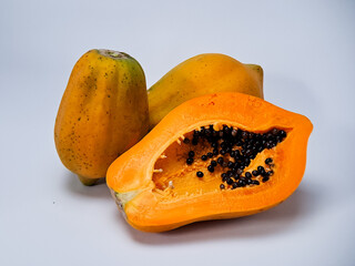 Three ripe papayas, one halved to showcase orange flesh and dark seeds, on a white backdrop.