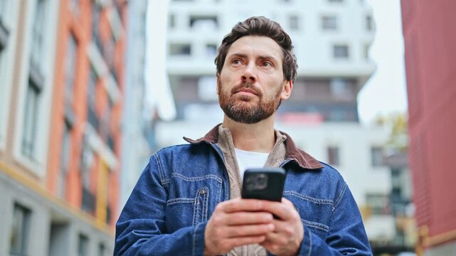 Man engages with smartphone technology outdoors, expressing initial focus, contemplation, then joy and pleasure from interaction. Urban setting in background.