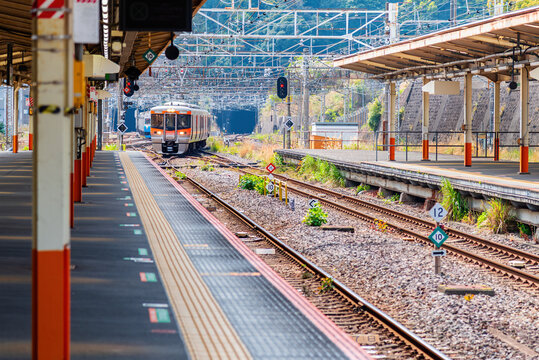 A local Japanese train is arriving at an empty rural station platform. Public transportation and travel in Japan concept, with railway tracks leading into the background.