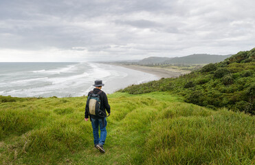 Man walking on green hillside. Unrecognizable people at Muriwai Beach. Auckland.