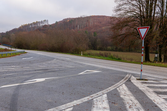 Empty rural road with yield traffic sign and autumn hills in background. Countryside intersection on cloudy day.