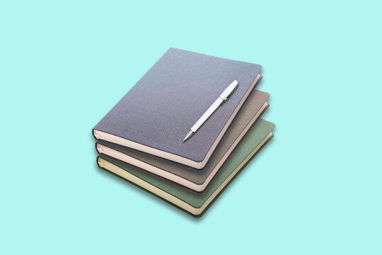 Stylish stack of modern notebooks with a sleek pen poised for writing, perfect for planning your success and capturing brilliant ideas in a clean, organized workspace.