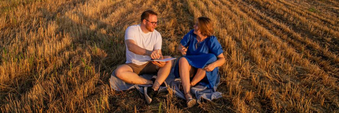Autumnal picnic brainstorming, Caucasian couple strategizing under golden sunset, celebrating upcoming Lughnasadh and whimsical penmanship day