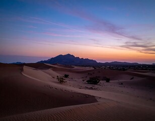 A serene desert landscape at dusk. Soft light paints dunes, mountains, and a clear sky, showing a peaceful evening after sunset