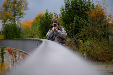 Woman taking photo with smartphone on autumn pedestrian bridge