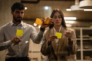 Business colleagues brainstorming ideas on glass wall with sticky notes