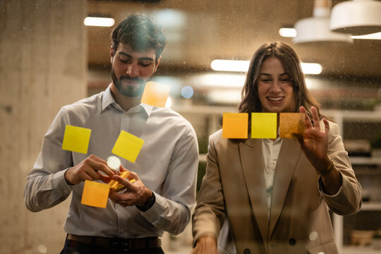 Business people brainstorming ideas on glass wall with sticky notes - Powered by Adobe