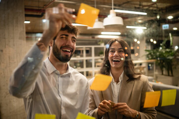 Colleagues brainstorming ideas using sticky notes on glass wall