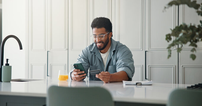 Happy, man and phone with credit card in kitchen for online shopping, easy transaction and payment. Ecommerce, person or smile with banking app in home for debit purchase, virtual checkout or fintech