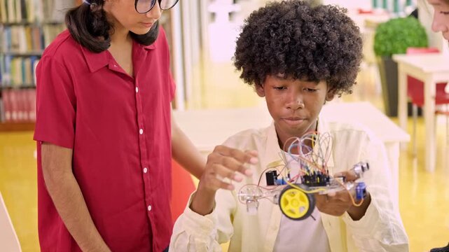 Indian, African, and mixed Asian-Caucasian students collaborate in a classroom, assembling a wheeled robot with wires and parts, engaging in hands-on STEM education, teamwork, and programming.