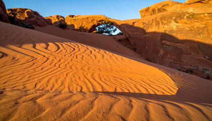 Desert landscape with a natural arch and rippled sand dunes.