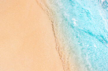 The image shows a close-up of sea foam rolling onto a sandy beach. The clear dividing line between the foam and the sand creates a minimalist and abstract visual effect.