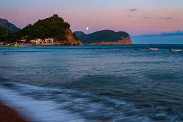City beach and sea at sunset, panorama of the resort town with embankment and architecture and moon in evening sky