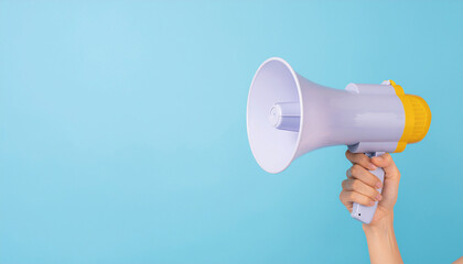 A hand holding a purple and yellow megaphone, ready to make an announcement or call attention, against a bright blue background with copy space.