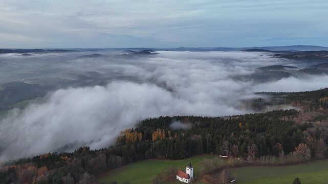 Drone view over the Bavarian Forest in Straubing Bogen showing foggy trees glowing in warm evening light and a calm autumn landscape in Bavaria