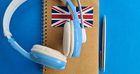Blue Headphones and a Notebook With a British Flag on a Blue Surface