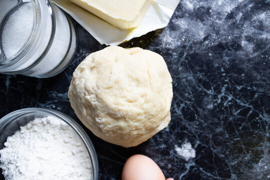 Raw dough and classic baking ingredients — flour, eggs, butter, sugar — on a dark rustic table. Top view. Homemade cooking and pastry preparation concept. - Powered by Adobe