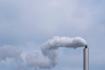 Tall smokestack emitting steam and vapor against a soft sky with thick cloud formations, highlighting metal details and infrastructure elements within an active industry environment 
