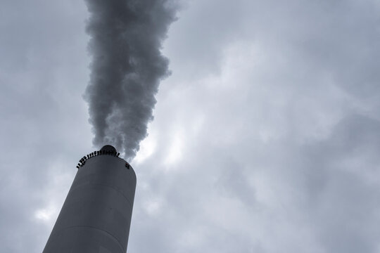 Industrial smokestack emitting steam and vapor into a textured sky with dense cloud formations, highlighting metal surfaces and infrastructure within a modern industry 