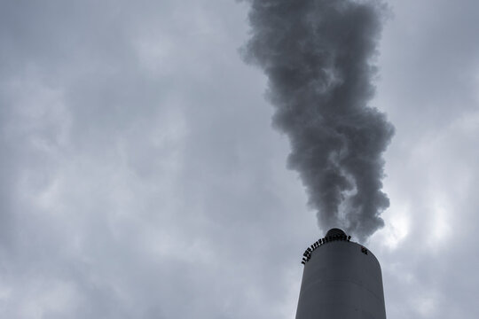 Closeup of a smokestack releasing steam and vapor into the sky, with cloud layers and metal details visible in an industry environment under heavy overcast conditions and subdued atmospheric lighting