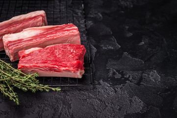 High-quality meat preparation. Raw beef cut with herbs and spices on a black textured background. Copy space provided.