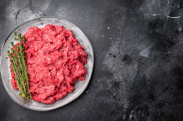 Raw ground wild game meat rabbit hare on a textured grey plate with fresh thyme, set on a dark, moody stone background.