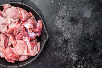 Fresh poultry duck offal in a black skillet, minimalist dark background highlights the raw product